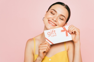 brunette young woman with closed eyes holding gift card isolated on pink